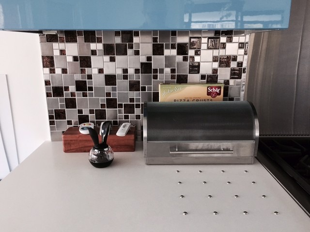 White concrete countertop with integral stainless steel trivets in front of grayscale tile backsplash. 