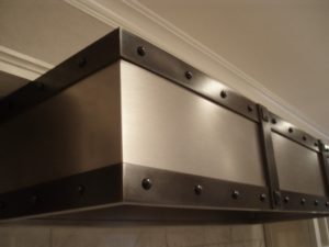 Custom vent hood made to go under kitchen cabinets. The body of the hood is brushed stainless steel and the frame is blackened stainless steel.