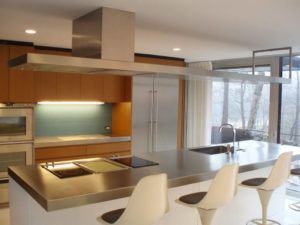 Sleek stainless steel kitchen hood mounted over an island cooktop and stainless steel countertop in a modern kitchen. 